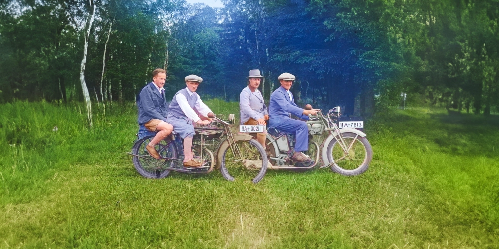 Vier Männer auf alten Mopeds vor einem Wald.